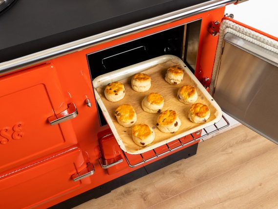 Een open ESSE fornuis met een bakplaat waarop versgebakken scones liggen, in een rode oven met een retro-uitstraling.