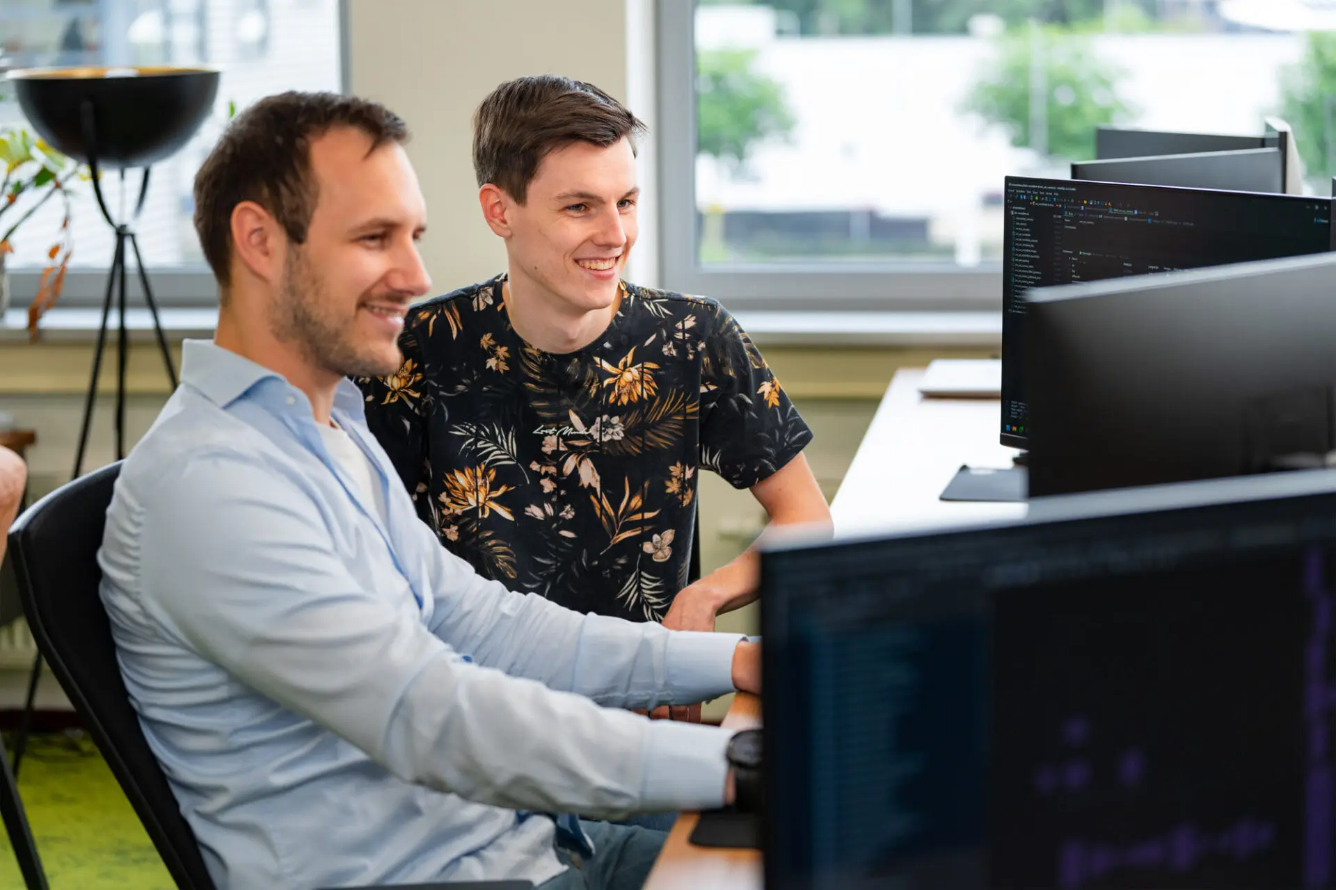 Twee mannen in overleg tijdens het werk achter hun computerschermen