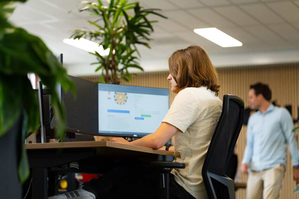 Man zit achter een bureau met drie schermen, waarvan er één aanstaat.