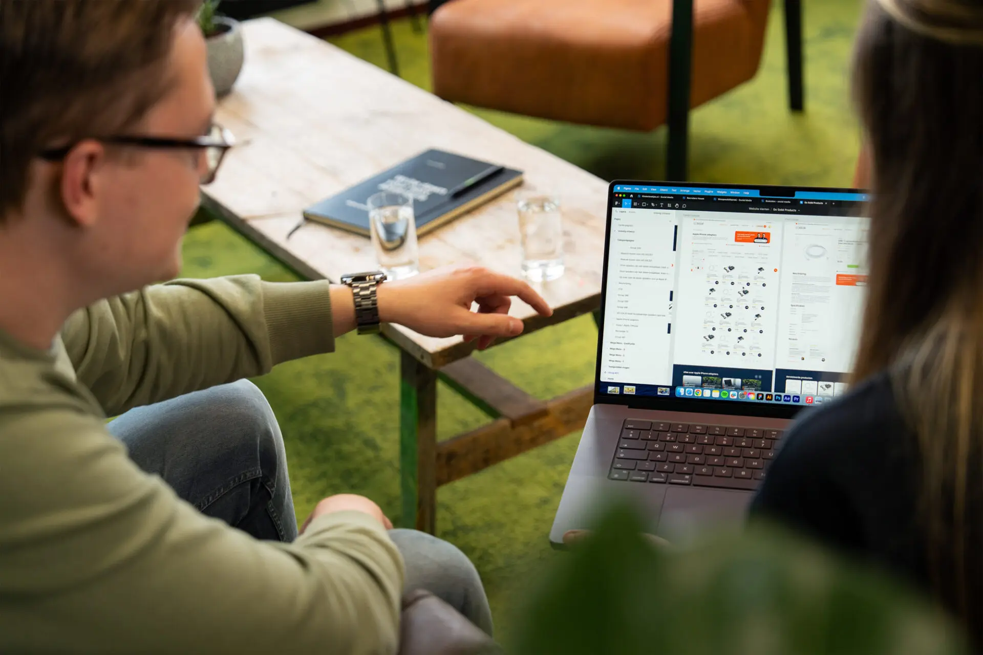 Man in groene trui wijst iets aan op laptop van zijn collega