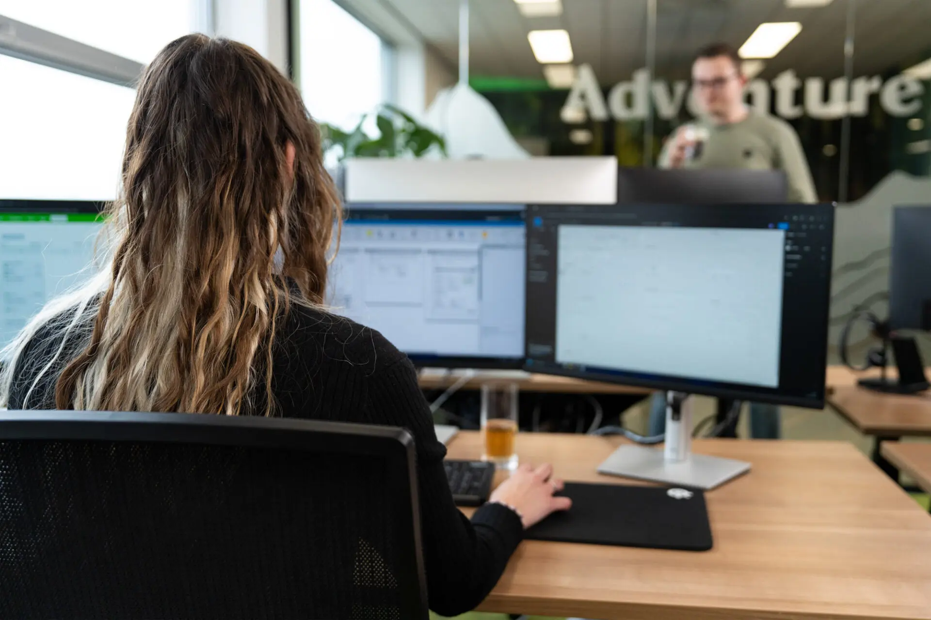 Dame zit achter haar bureau te werken met drie computer schermen