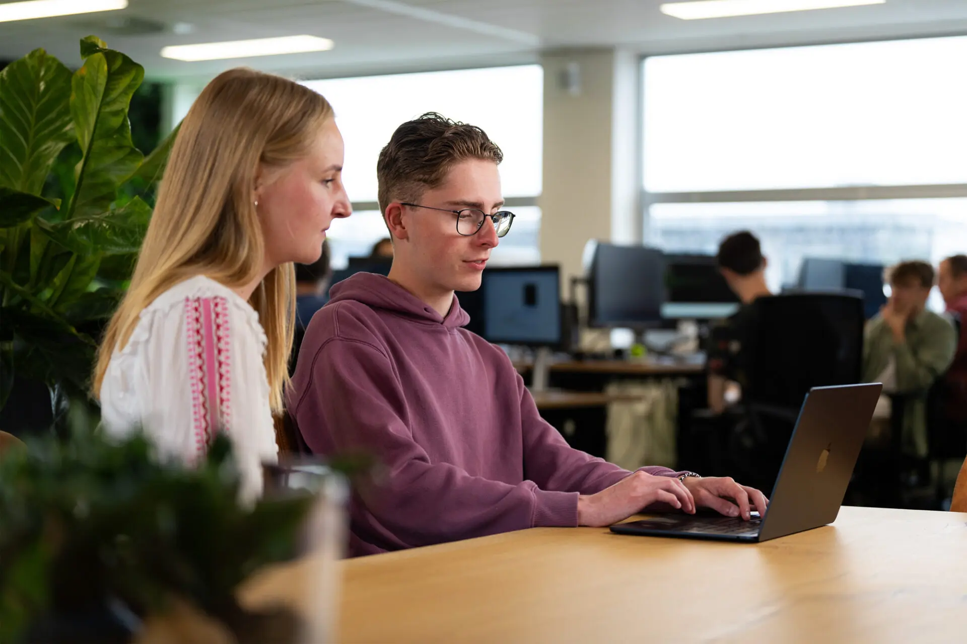 Man zit achter laptop en toont een AI-agent aan vrouw in wit shirt die ernaast zit.