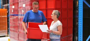 Magazijnmedewerkers bespreken logistieke details met rode kunststof bakken op de achtergrond.