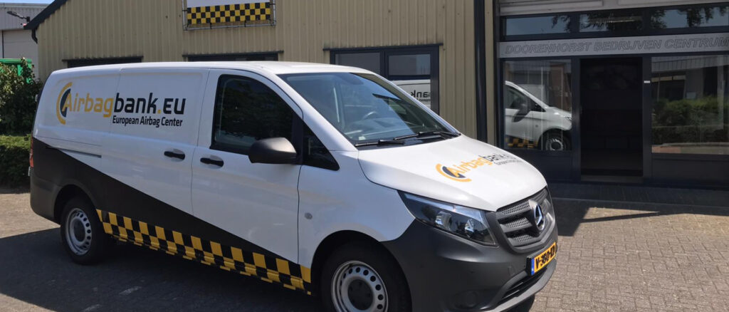 Een witte Mercedes-Benz bedrijfswagen met Airbagbank.eu-logo en zwart-gele belettering, geparkeerd voor een bedrijfspand met bijpassende branding.