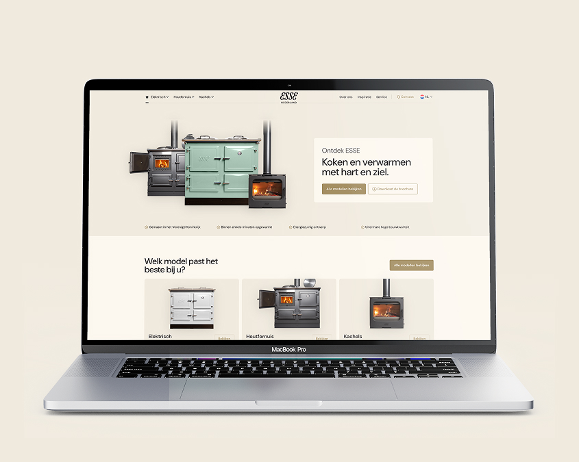 Een MacBook Pro met de homepage van de ESSE Cookers website, waarop verschillende fornuizen en kachels te zien zijn, met een focus op koken en verwarmen met een traditioneel design.