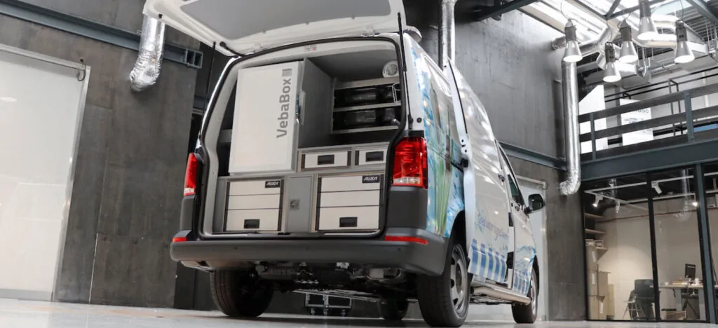 Een bestelwagen met open achterdeuren in een industriële ruimte, waarin een VebaBox-koelunit en opberglades zijn ingebouwd