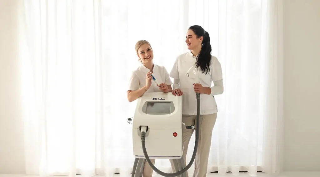 Twee huidtherapeuten in witte uniformen poseren met een professionele medische huidbehandelingsmachine in een lichte ruimte.