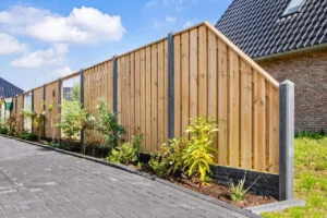 Een moderne houten schutting met antracietkleurige palen in een tuin met beplanting.
