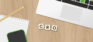 Houten bureau met rechtsboven een gedeeltelijk zichtbare laptop, linksonder een smartphone met groene rand, daarnaast een notitieblok en potlood, en in het midden drie houten letterblokjes met de letters ‘CRO’.