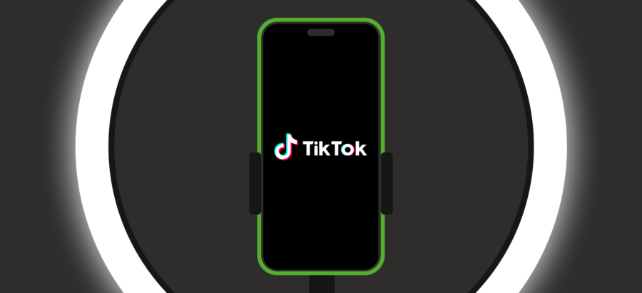 Een smartphone met een groen randje is bevestigd in een houder voor een ringlamp en toont het TikTok-logo, wat een setting suggereert voor het maken van content.
