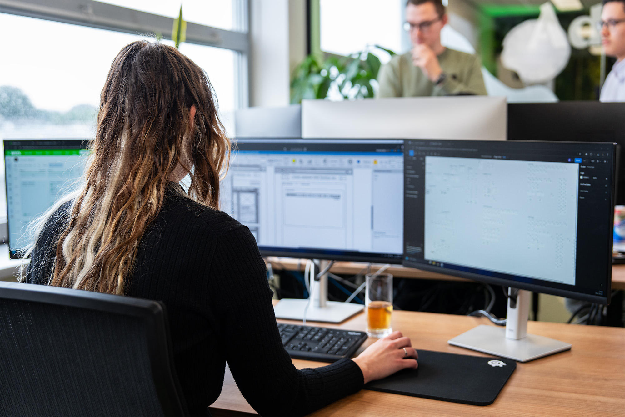 Medewerker werkt gefocust met meerdere schermen aan AI-marketing in een moderne kantooromgeving, terwijl collega's op de achtergrond samenwerken.
