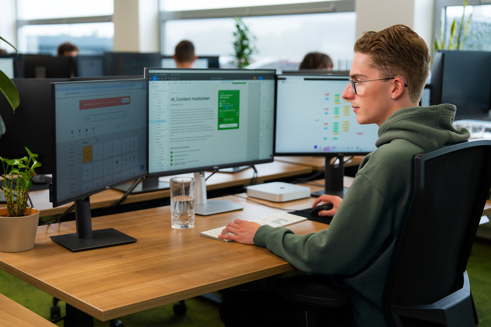 Jonge marketeer analyseert AI-gegenereerde content en dashboards op meerdere schermen binnen een open kantoorruimte, met focus op marketing.