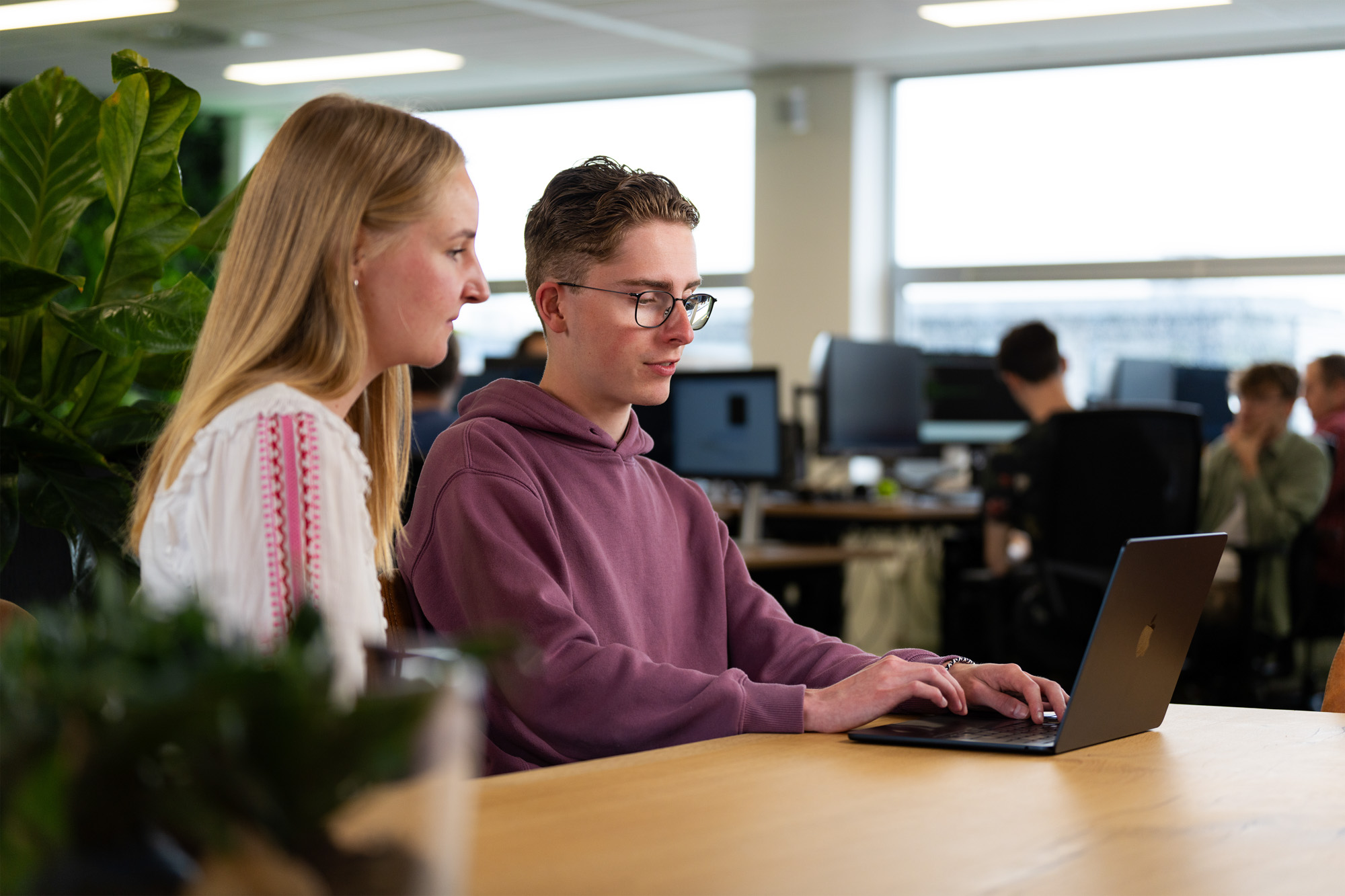 Twee collega’s overleggen over AI-gegenereerde content op een laptop in een open kantoorruimte, gericht op creatieve samenwerking en slimme contentoptimalisatie.