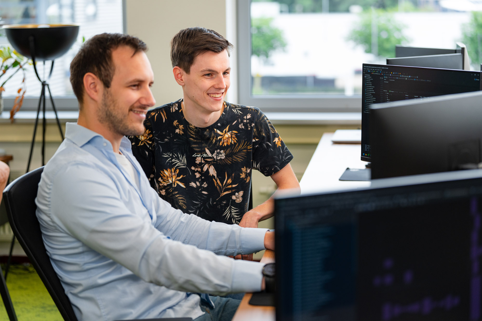 Twee collega’s werken samen achter meerdere computerschermen aan de ontwikkeling en implementatie van een ERP-systeem.