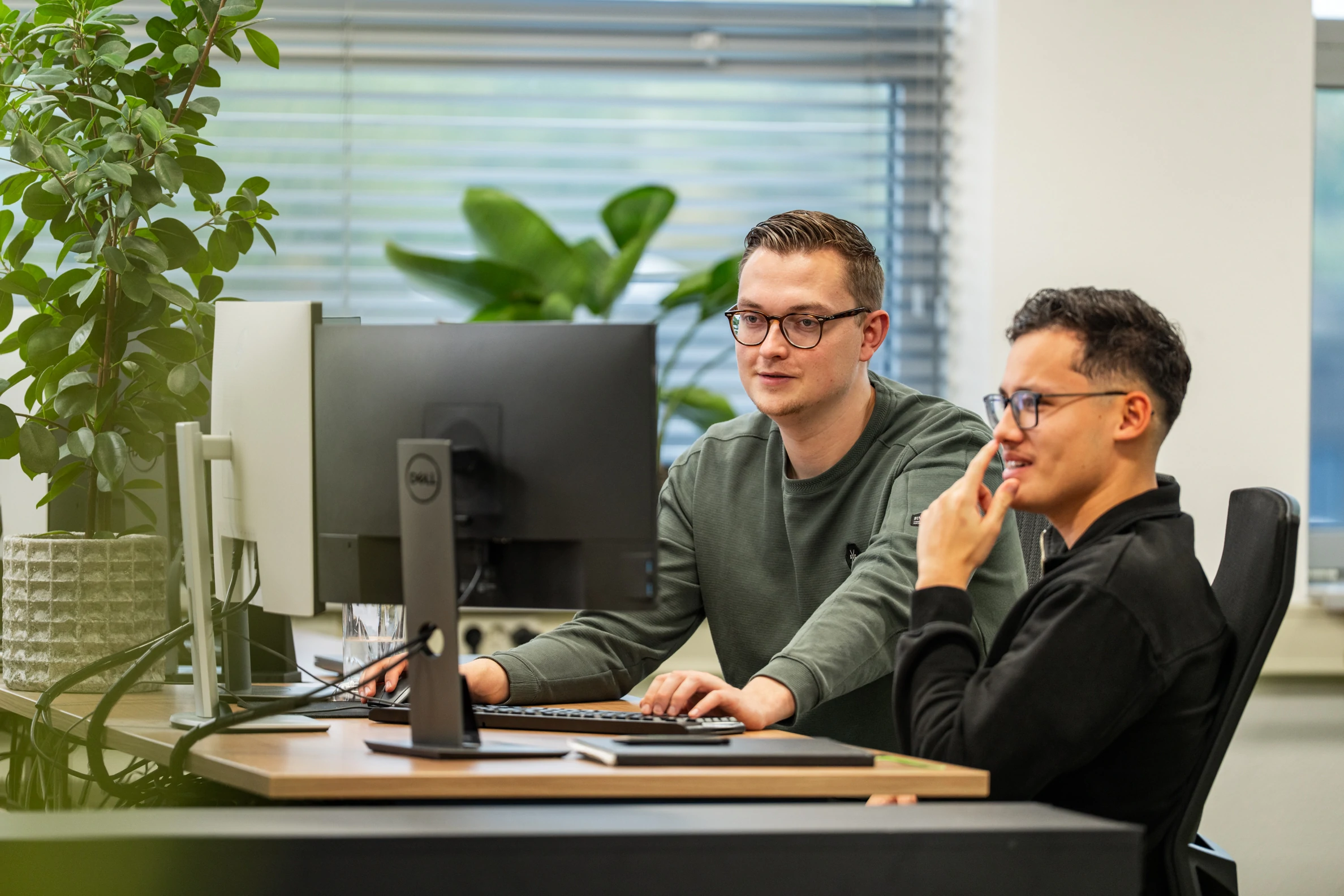 Twee collega’s werken samen achter dubbele beeldschermen aan configurators in het moderne kantoor van Wux.