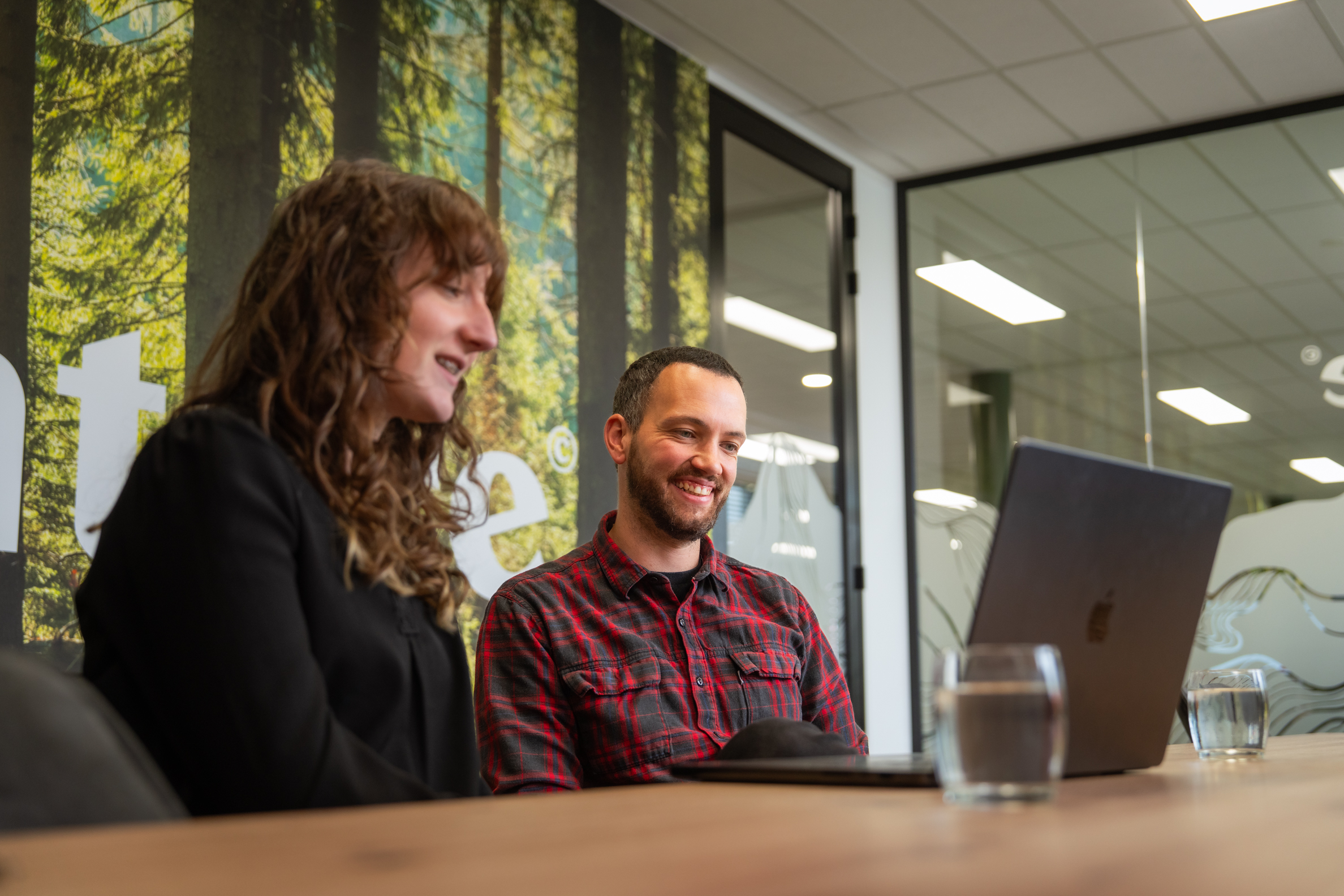 Twee collega’s lachen tijdens een overleg over SEA achter een laptop in een vergaderruimte