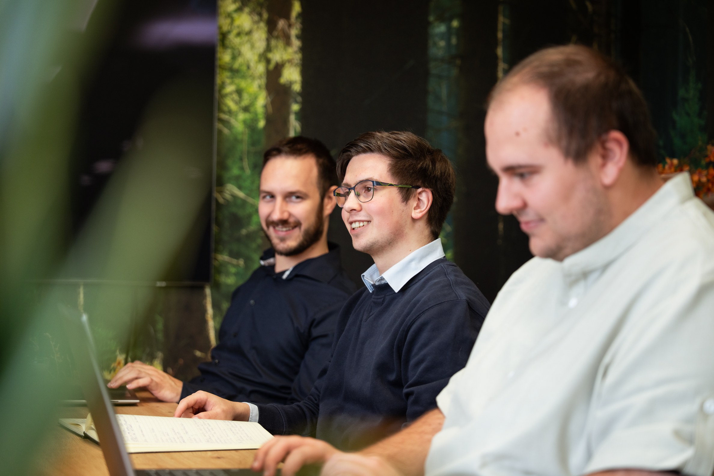 Drie collega’s zitten samen aan tafel met laptops en notities tijdens een teamoverleg over online strategie op kantoor.