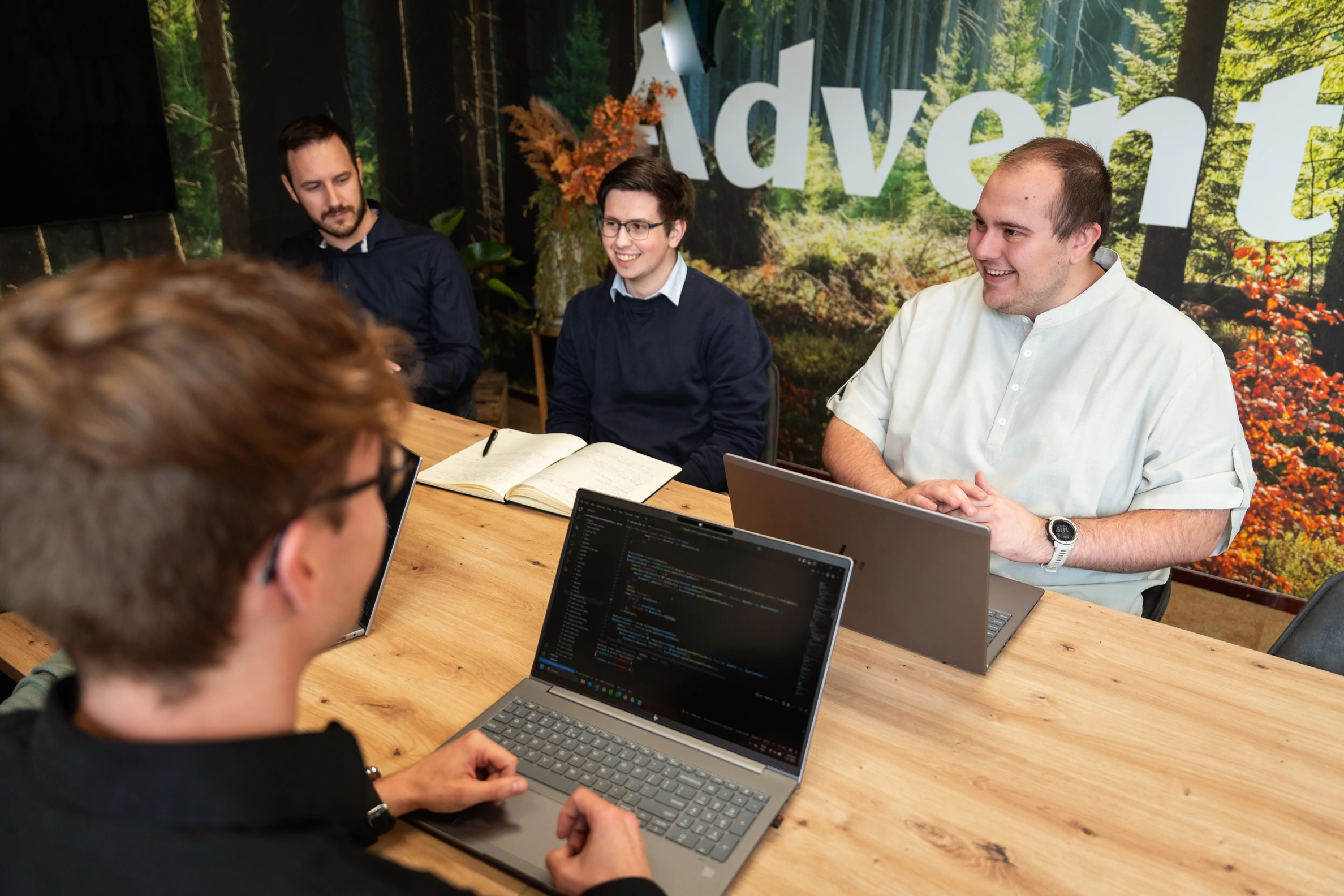 Vier collega’s overleggen aan tafel met laptops en notitieboekjes in een vergaderruimte.