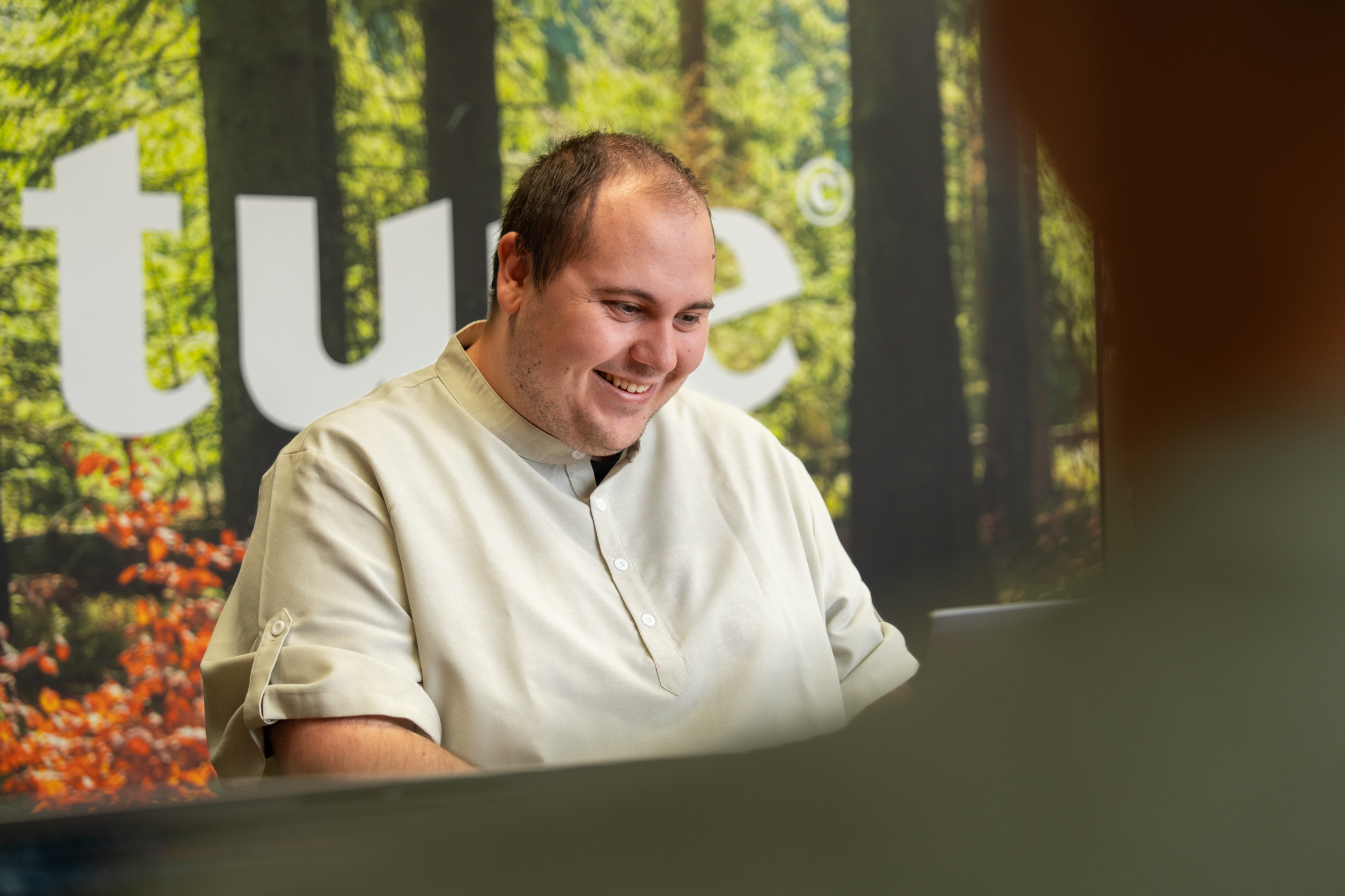 Man glimlacht terwijl hij aan zijn laptop werkt in de kantoorruimte van Wux.