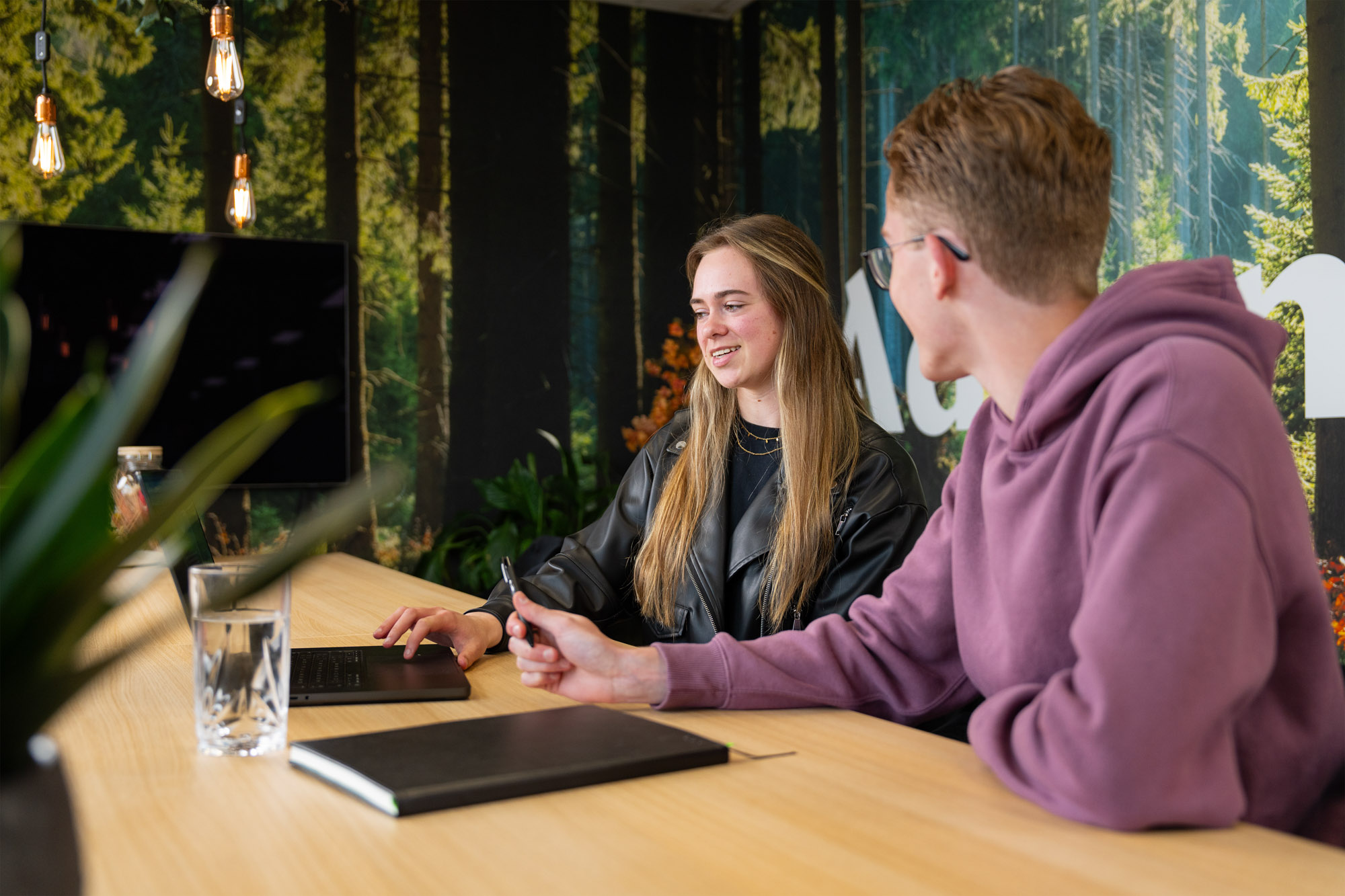 Twee collega’s van Wux bespreken het design en de functionaliteiten van een nieuwe applicatie tijdens een overleg aan tafel.