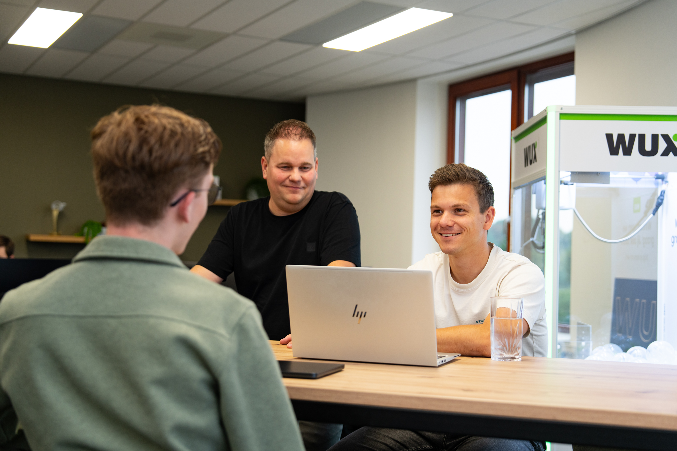 Drie collega’s van Wux bespreken wireframes tijdens een websiteproject aan tafel met een laptop.