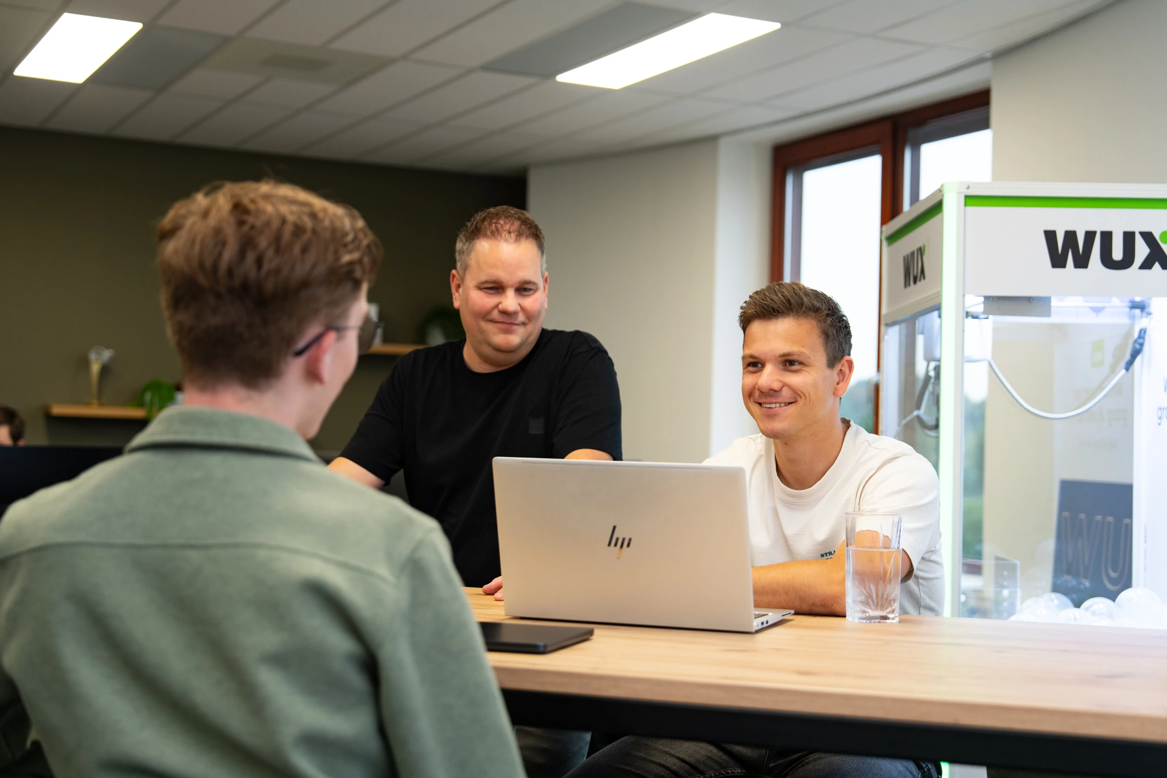 Drie collega’s van Wux bespreken wireframes tijdens een websiteproject aan tafel met een laptop.