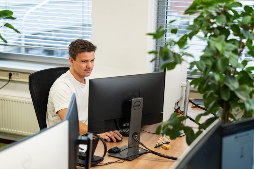 Ontwikkelaar van Wux werkt achter een bureau op meerdere computerschermen aan een CRM systeem
