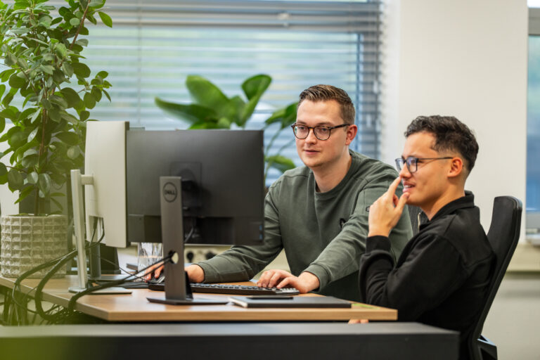 Twee developers van Wux analyseren API-monitoringgegevens op meerdere schermen om koppelingen te optimaliseren.