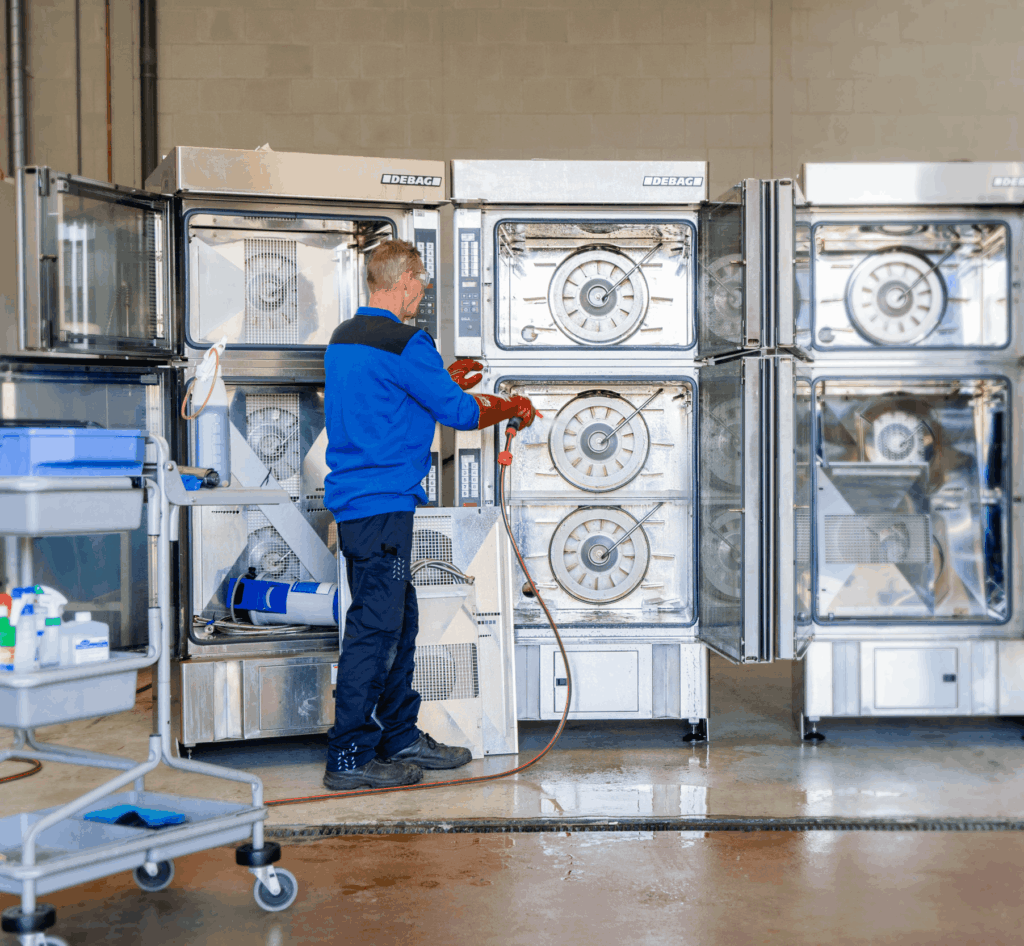 Grondige reiniging in actie: een zweegers medewerker en beschermende handschoenen maakt met een hogedrukspuit de binnenkant van grote, industriële ovens van het merk Debag schoon.
