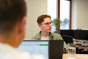 Collega’s van Wux overleggen achter laptops over websitebeheer en webhosting in een moderne kantooromgeving.