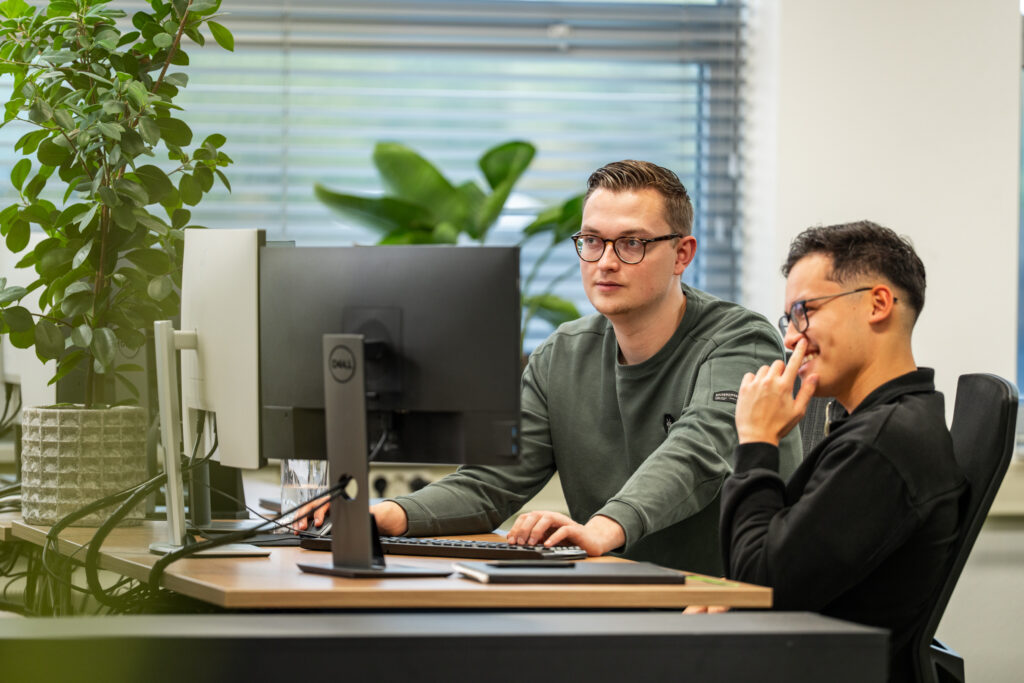 Twee ontwikkelaars van Wux werken gezamelijk op één computer aan de ontwikkeling van een PIM-systeem