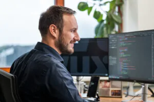 Developer van Wux bekijkt code op meerdere schermen, symbool voor de techniek en infrastructuur achter betrouwbare webhosting.