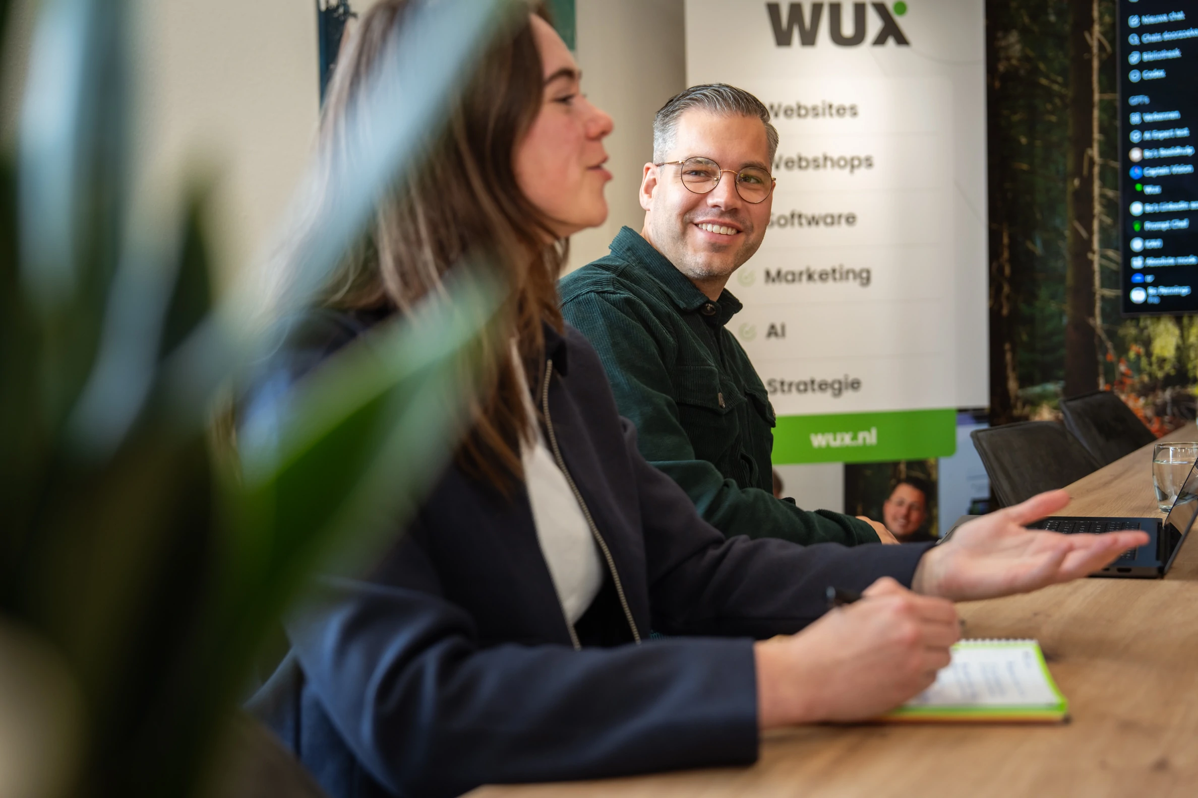 Twee collega’s van Wux overleggen in een moderne kantooromgeving over de strategische aanpak bij het bouwen van websites.