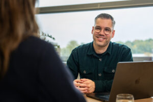 Consultant van Wux in gesprek met klant over AI en social advertising strategie aan tafel met laptop.
