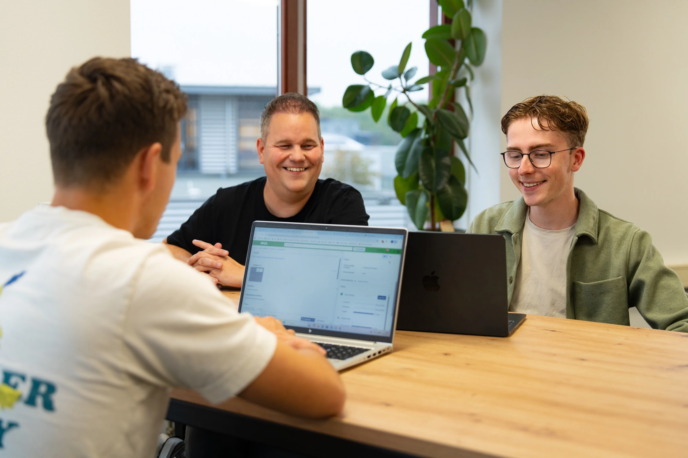 Drie collega's van Wux overleggen aan tafel met hun laptops over de overstap van iDEAL naar Wero.