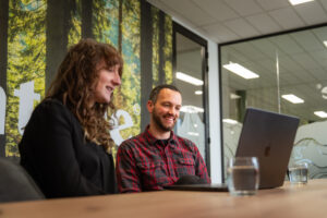 Twee specialisten van Wux overleggen lachend voor een laptop over de inzet van AI-assistenten.