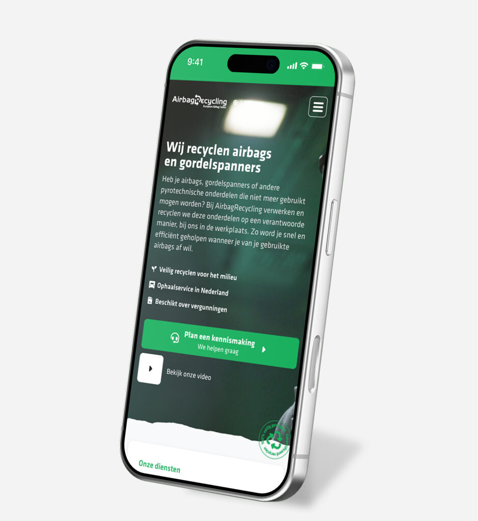 Een schuine opname van een smartphone met de groene mobiele website van AirbagRecycling. Op het scherm staat de koptekst "Wij recyclen airbags en gordelspanners" met een lijst van voordelen, een opvallende groene knop "Plan een kennismaking", en een link naar een video.