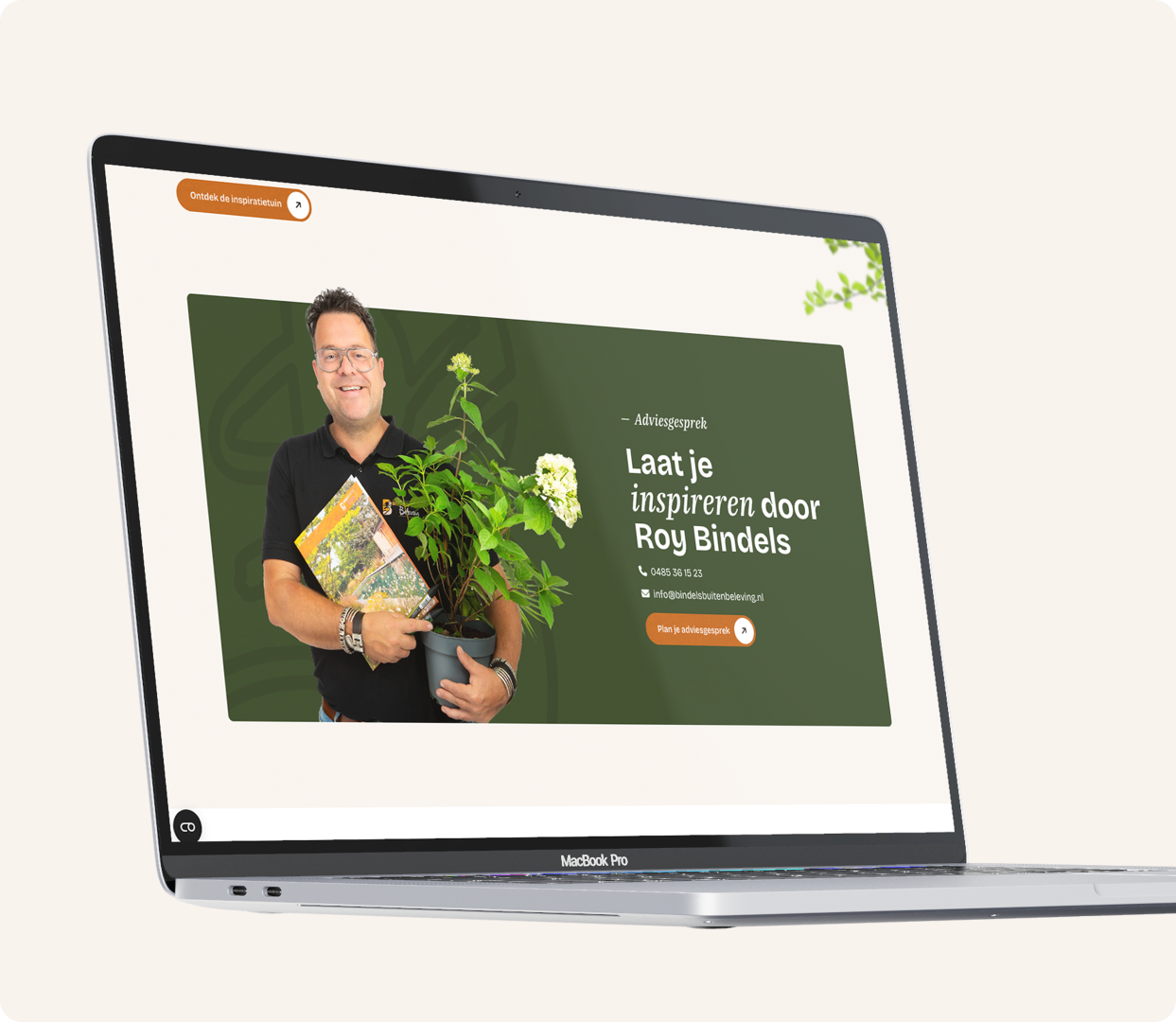 Een schuin afgebeelde MacBook Pro die een sectie van de Bindels Buiten Beleving website toont voor het aanvragen van een adviesgesprek. Op het scherm staat een groene banner met de tekst "Laat je inspireren door Roy Bindels", contactgegevens en een oranje knop om een gesprek te plannen. Naast de tekst staat een uitsnede van Roy Bindels die lachend een plant met witte bloemen en een brochure vasthoudt.