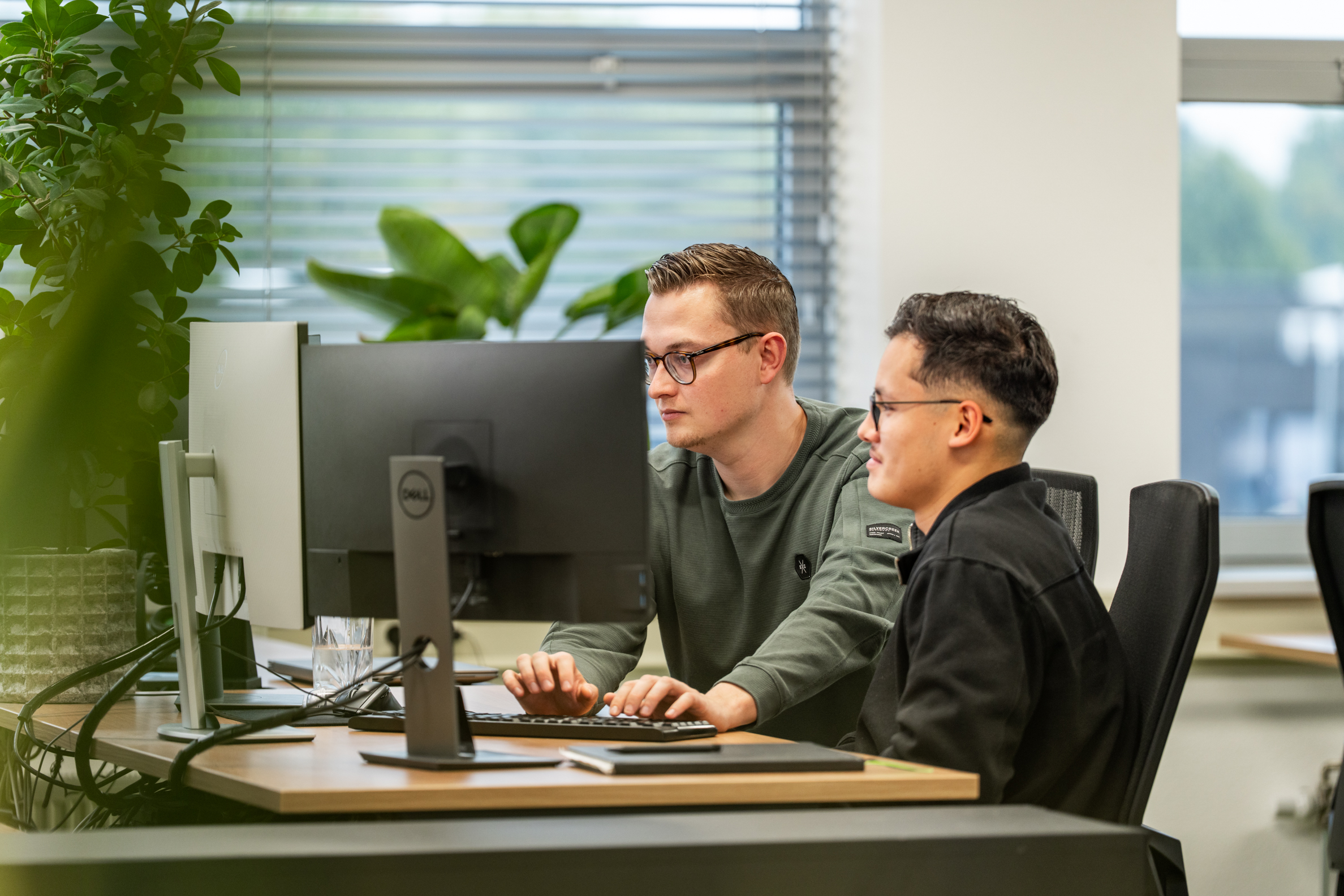 Twee Wux-medewerkers werken samen achter meerdere beeldschermen aan de implementatie van het CRM-opschoonproces.